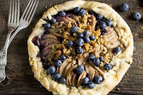 rustic pear and blueberry galette on board table with two antique silver forks to the left