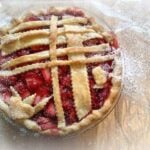 overhead shot of strawberry pie with pie crust lattice and sprinkled with powdered sugar, sitting on parchment paper