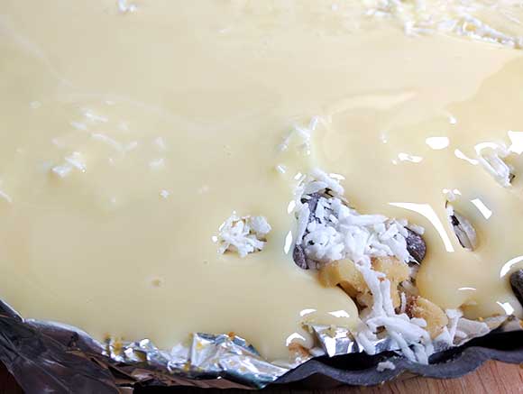 sweetened condensed milk is poured over top all of the ingredients before baking