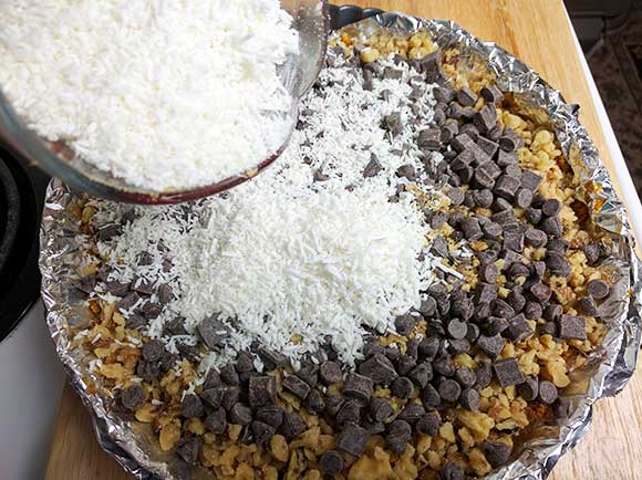 layering the coconut flakes on top of the chocolate chips for the seven layer bar or magic cookie bar recipe