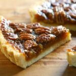 A slice of pecan pie on a wooden cutting board.