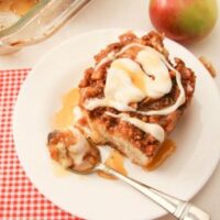 big slice of apple pie coffee cake on a white plate, with spoon, walnuts and apple to the side