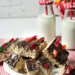 gummy worm treats with chocolate icing topped with gummy worms on a white plate on top of red white checked cloth