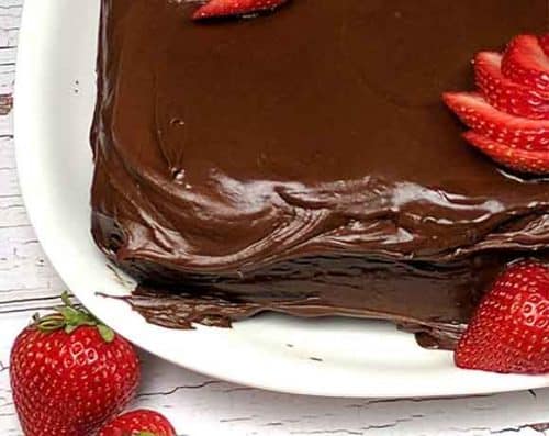 square chocolate cake corner with sliced strawberries on a white square plate
