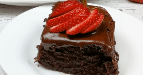 small piece of chocolate cake on a white plate with a sliced strawberry fanned on top of chocolate buttercream icing