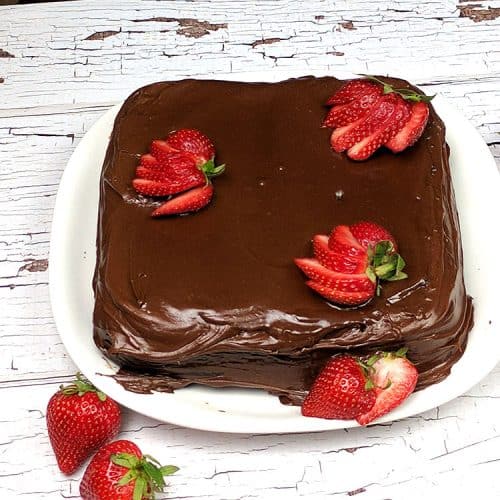 hocolate Mayonnaise Cake square on a white plate on white wooden table with sliced strawberries arranged on top and side