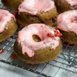 closeup image of strawberry donuts with pink strawberry icing cooling on a baker's rack