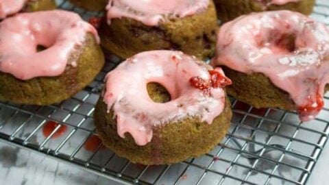 closeup image of strawberry donuts with pink strawberry icing cooling on a baker's rack