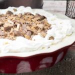 Ice cream pie in a red pie plate with chocolate and toffee bits sprinkled on top with whipped cream