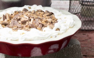 Ice cream pie in a red pie plate with chocolate and toffee bits sprinkled on top with whipped cream