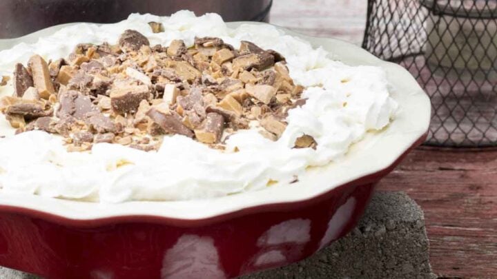 Ice cream pie in a red pie plate with chocolate and toffee bits sprinkled on top with whipped cream