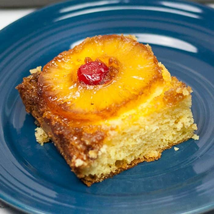 piece of pineapple upside down cake on blue plate with slice of pineapple and maraschino cherry on top, box cake mix hacks