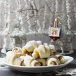 apricot jam rugelach cookies on a white plate in front of a white decorative tree with a dreidel ornament