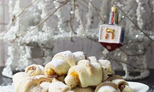apricot jam rugelach cookies on a white plate in front of a white decorative tree with a dreidel ornament