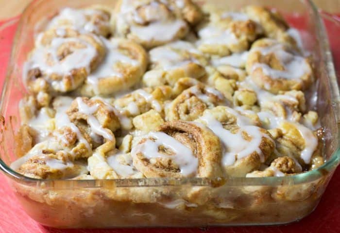 Cinnamon Swirl Apple Cobbler with white sugar glaze in a square glass baking dish on a red placemat