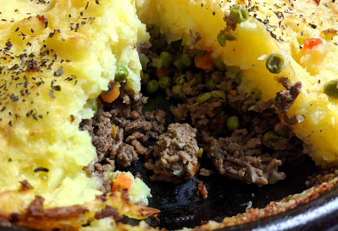 homemade shepherd's pie in cast iron skillet with two servings removed