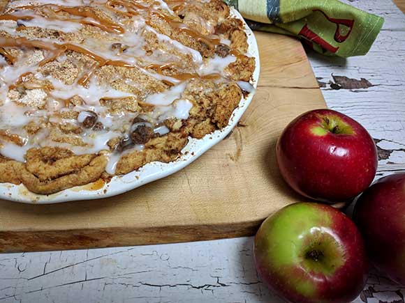 Dutch Apple Pie in white pie plate on printed tea towel with apples