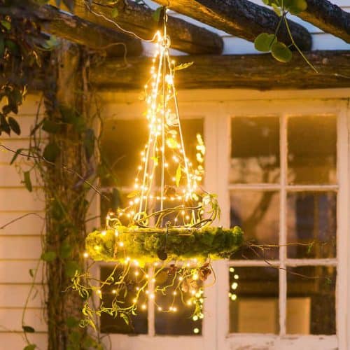 backyard chandelier, with circle of moss, frame is covered in fairy lights and hung from a gazebo, in front of a window, and vines growing on gazebo