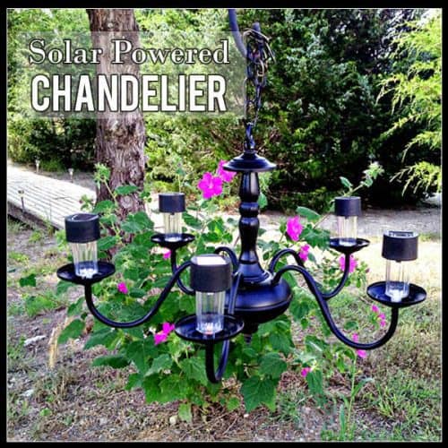 black iron chandelier with pink flours and trees in background and solar lights