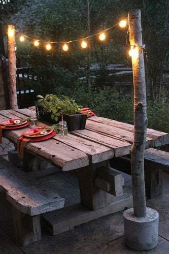 string lights are mini light bulbs strung between two tree posts and a wooden picnic table with plants and table settings