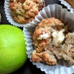 green apples with freshly baked apple muffin in muffin wrapper with melted butter on top more muffins in the background