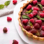chocolate tart with raspberries on top with single raspberries and mint leaves and grey napkin