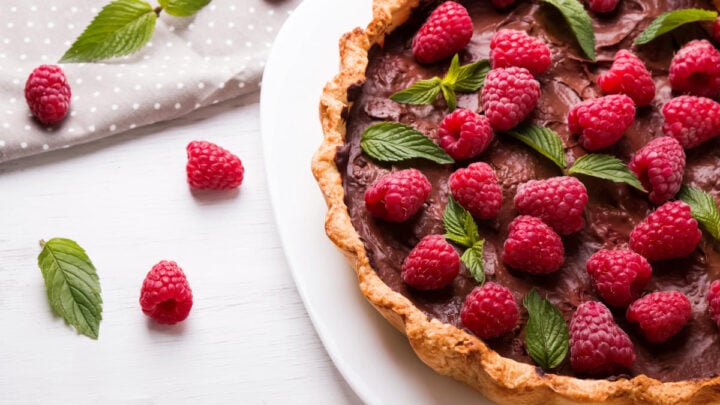 chocolate tart with raspberries on top with single raspberries and mint leaves and grey napkin
