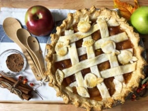 lattice topped apple pie with measuring spoons, cinnamon sticks, apples on a wooden board