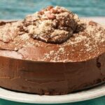 side view of chocolate fudge cake with chocolate buttercream icing and chocolate caramels and almonds on top