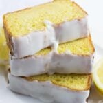 lemon loaf cake with white glaze icing, sliced on a white plate with lemons on the side,