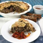 A meat pie on a plate with a slice taken out.