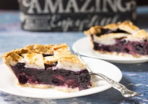 two pieces of pie on white plates with forks on blue background