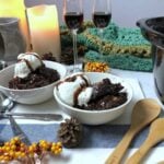 smores crockpot lava cake in two white bowls, with table decorations, candles and two wine glasses with kahlua