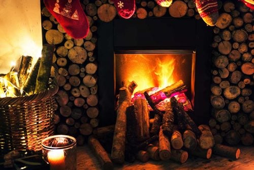 festive fireplace with decorated mantel, logs stacked to the left and a candle in the foreground