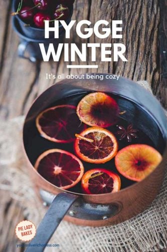 hygge winter in white text on image that shows copper pot full of mulled wine, sliced oranges floating on top, surface is barn board