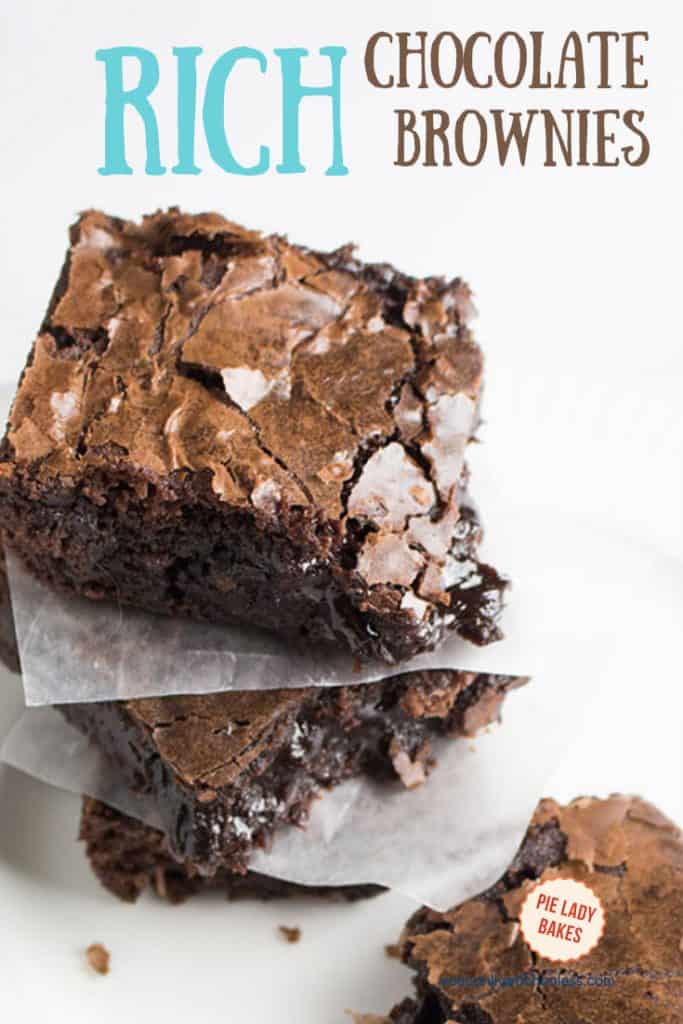 two brownies stacked on waxed paper with one gooey chocolate brownie to the right all on a white plate and text for pinning