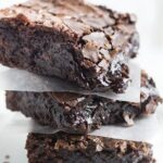three chocolate brownies stacked with parchment paper in between