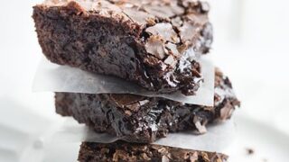 three chocolate brownies stacked with parchment paper in between