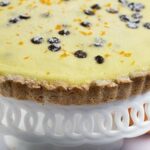 ricotta pie on white cake plate with scalloped edging and orange by pedestal to the right