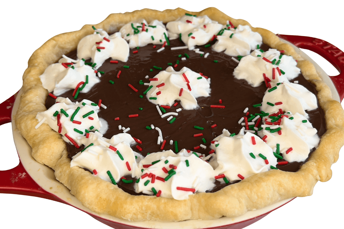 A homemade chocolate pie in a red dish, topped with dollops of whipped cream and red, green, and white sprinkles.