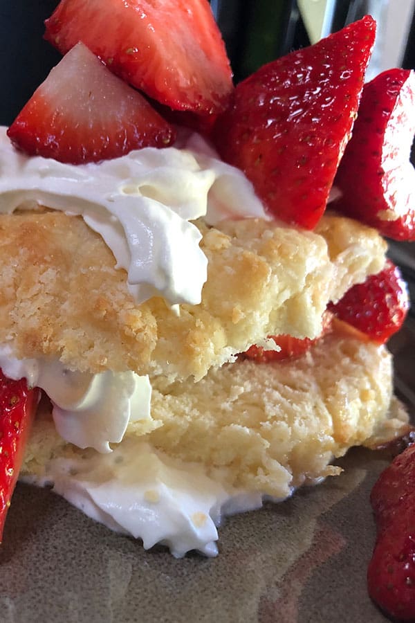 Close-up of a dessert with layers of shortcake, whipped cream, and sliced strawberries.