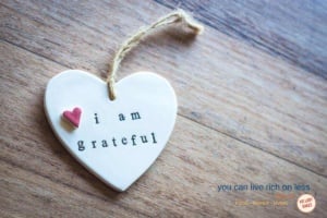 heart pendant with jute tied to it on a wooden table says i am grateful in small lower case type and a small pink heart attached