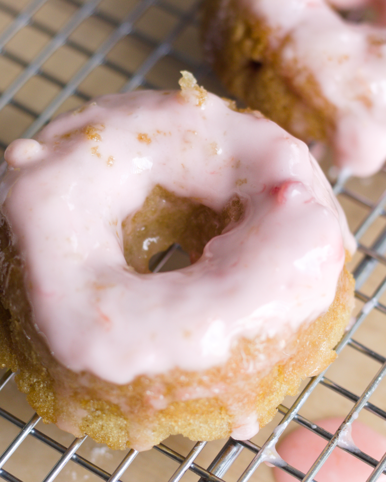 A close-up of a homemade donut with pink icing on a metal cooling rack, perfect for anyone craving delicious strawberry cake donuts.