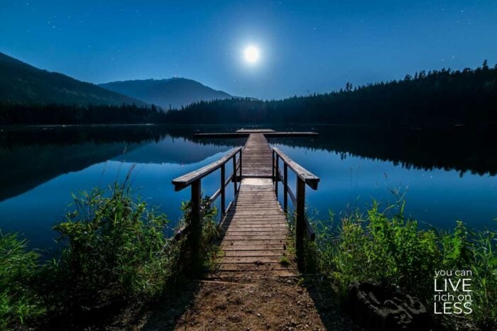 long dock over a lake with mountains in the background and a full moon in the sky