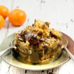 bread pudding with caramel sauce in a brown dish with two spoons and three mandarin oranges in the background