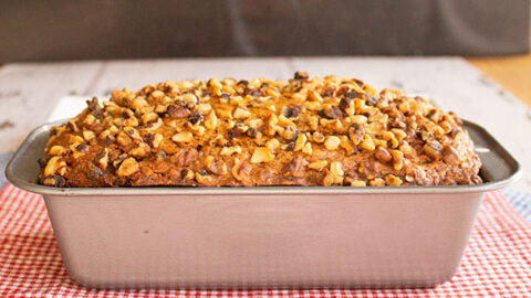 loaf of banana bread in a metal loaf pan on a white checked napkin