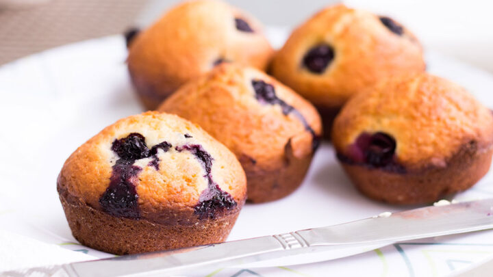 five blueberry muffins on a white napkin with knife