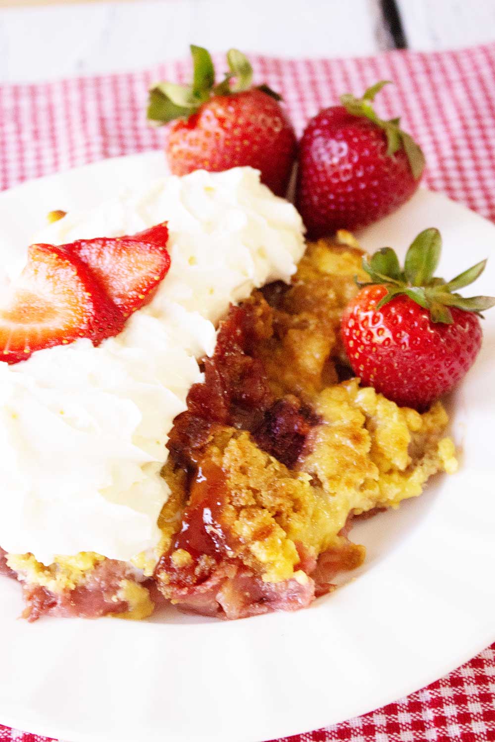 generous serving of strawberry rhubarb crumble with whipped cream and sliced strawberries on a white plate