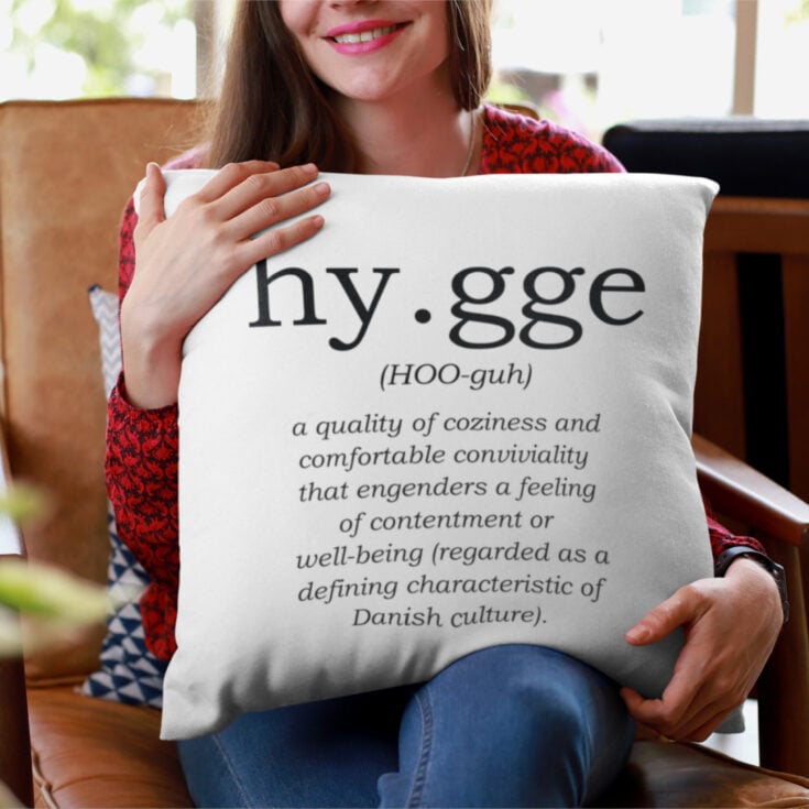 woman holding a pillow that has the definition of hygge printed on it