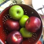 green and red apples in red colander on a printed tea towel with ingredients ready to make apple pie filling